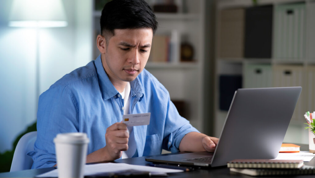 Man looking at his credit card while at a computer - payment redirection - Shift4